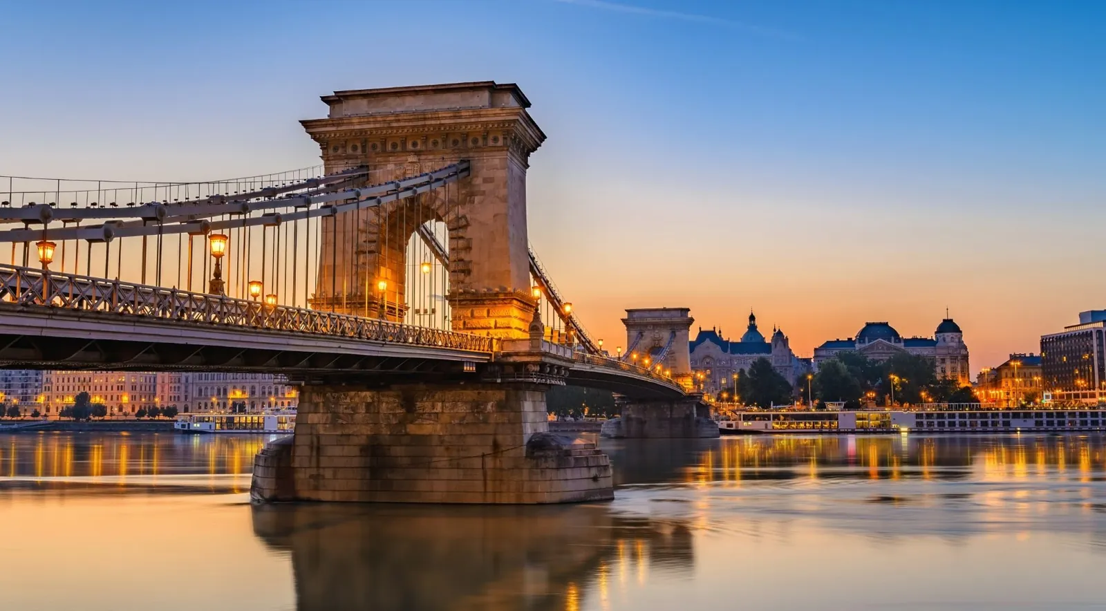 The stone towers of the Chain Bridge lit at dusk over the river