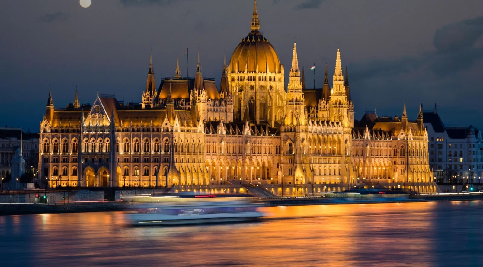 The Hungarian Parliament floodlit at night on the Danube, a boat's light trail across the water