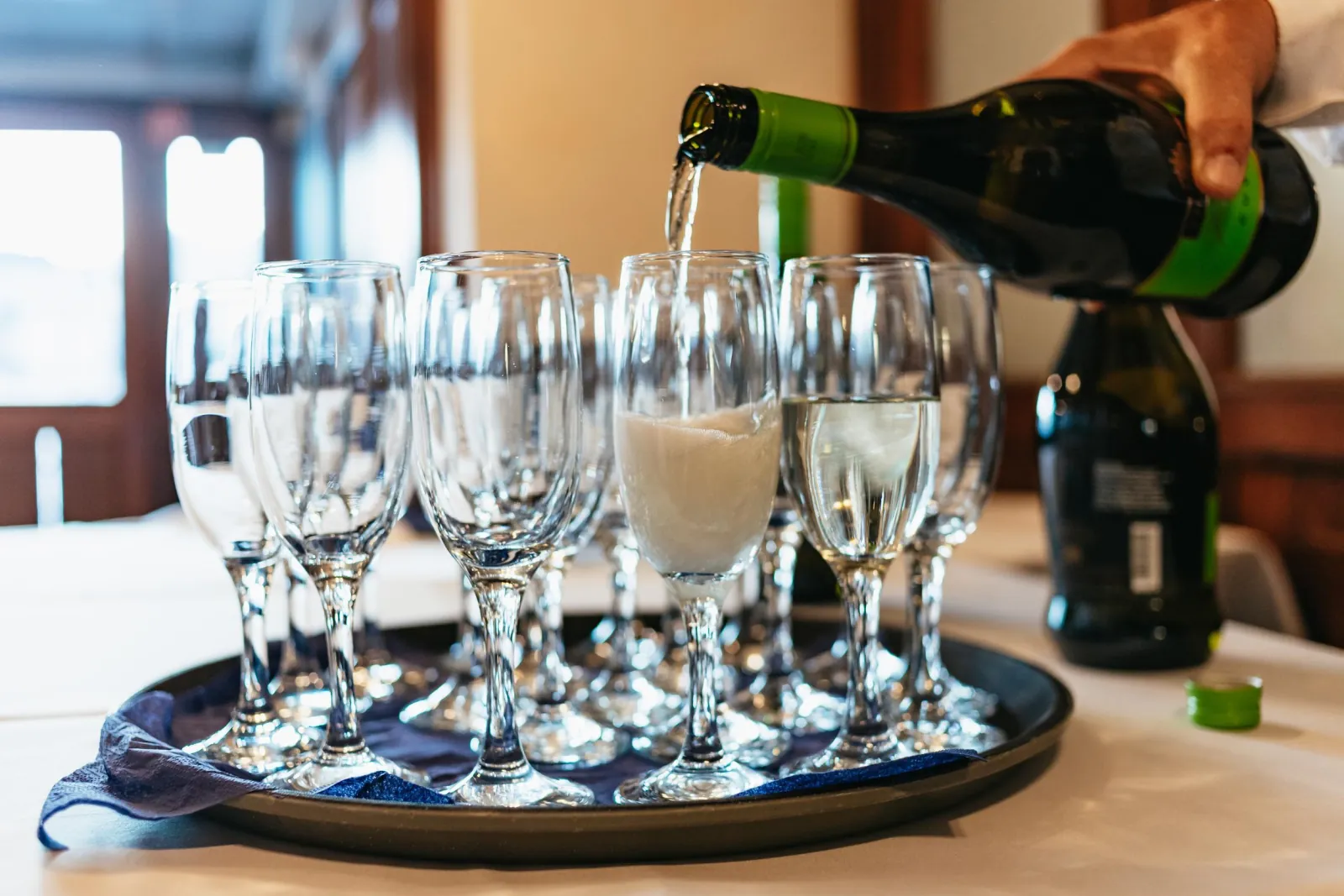 A waiter pouring sparkling wine into a tray of glasses