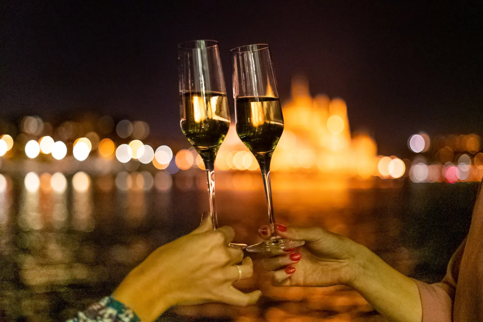 Two glasses of sparkling wine raised against the lights of the river