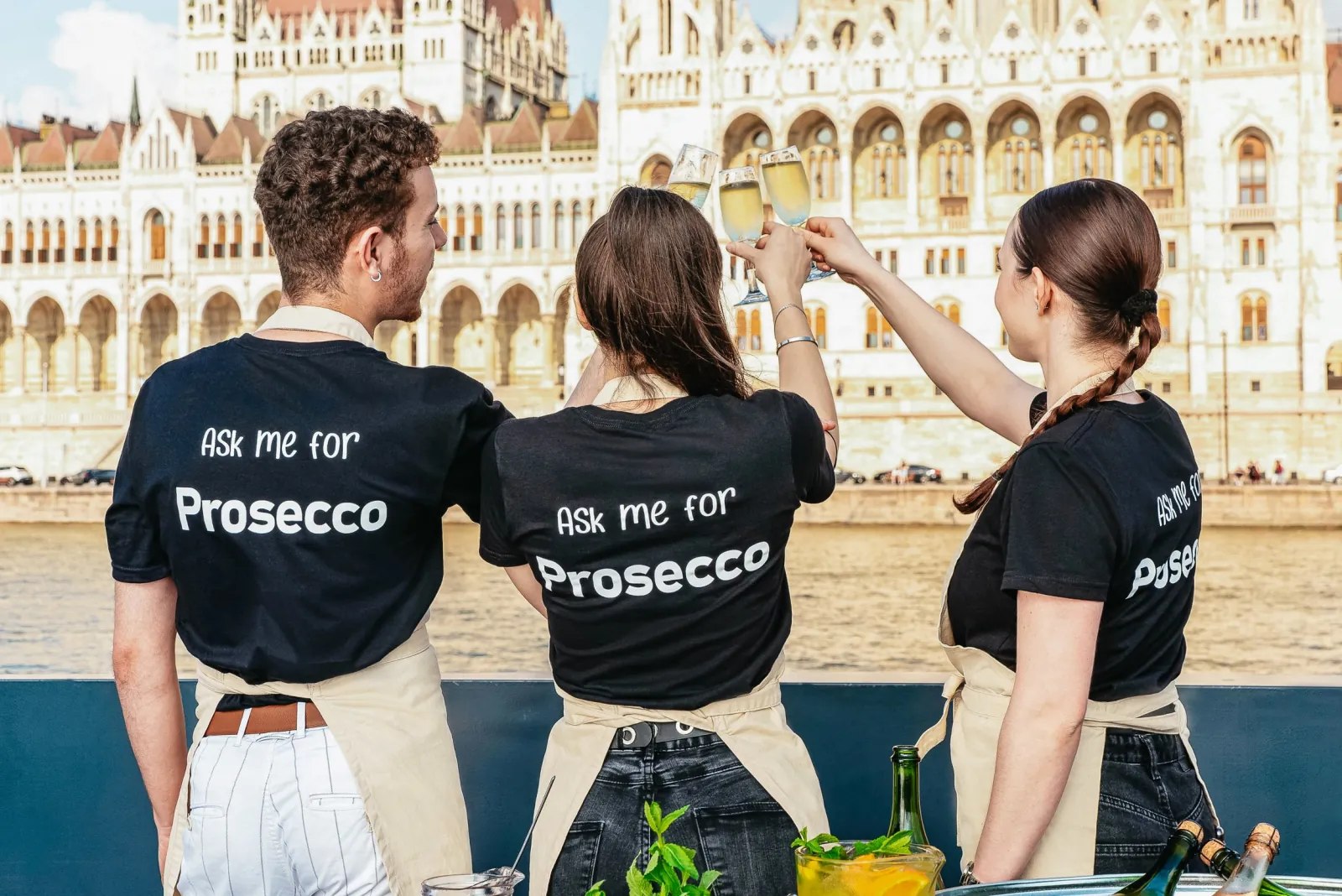 Crew in “Ask me for Prosecco” shirts on deck facing the Parliament