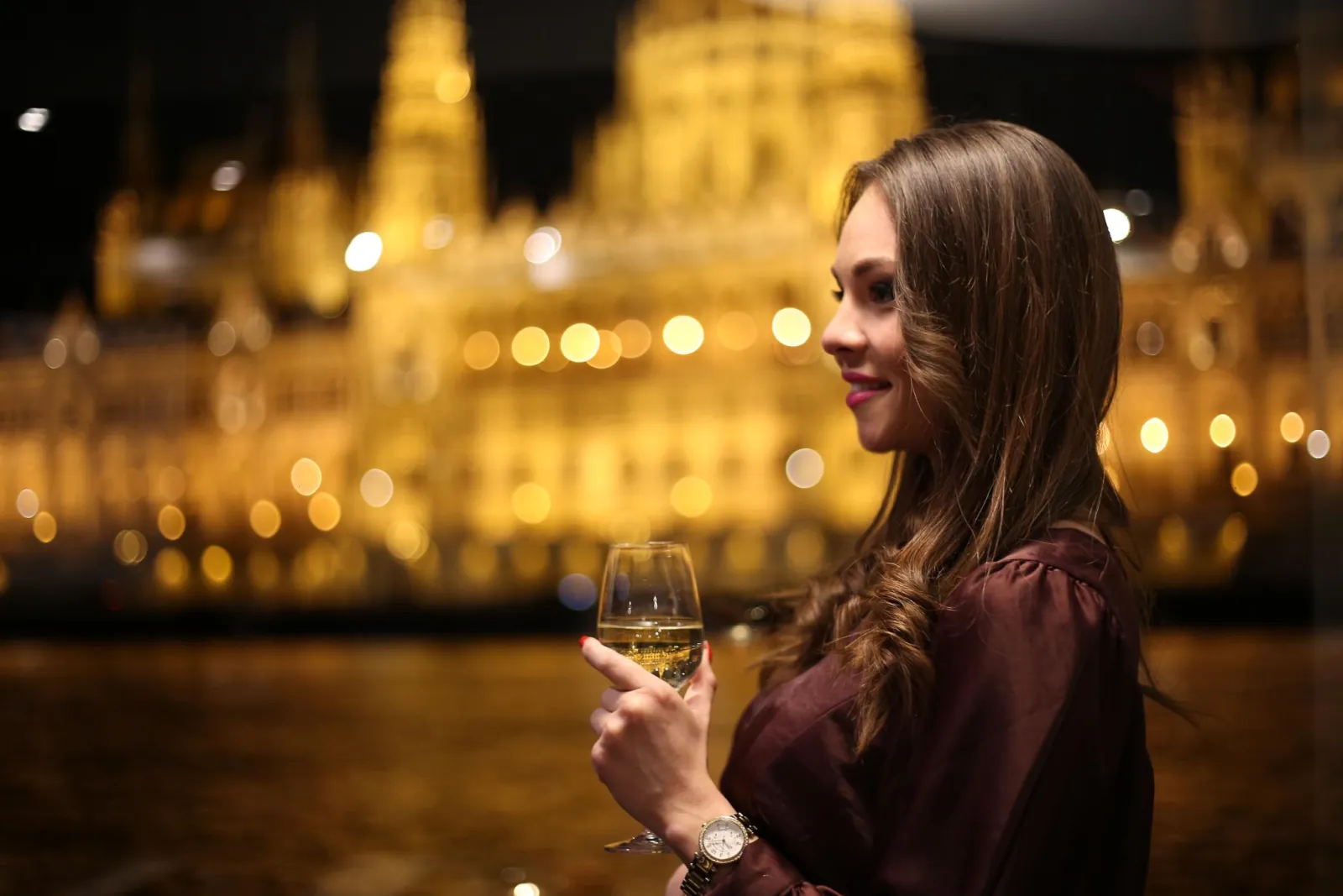A guest holding a glass of wine against the lights of the river