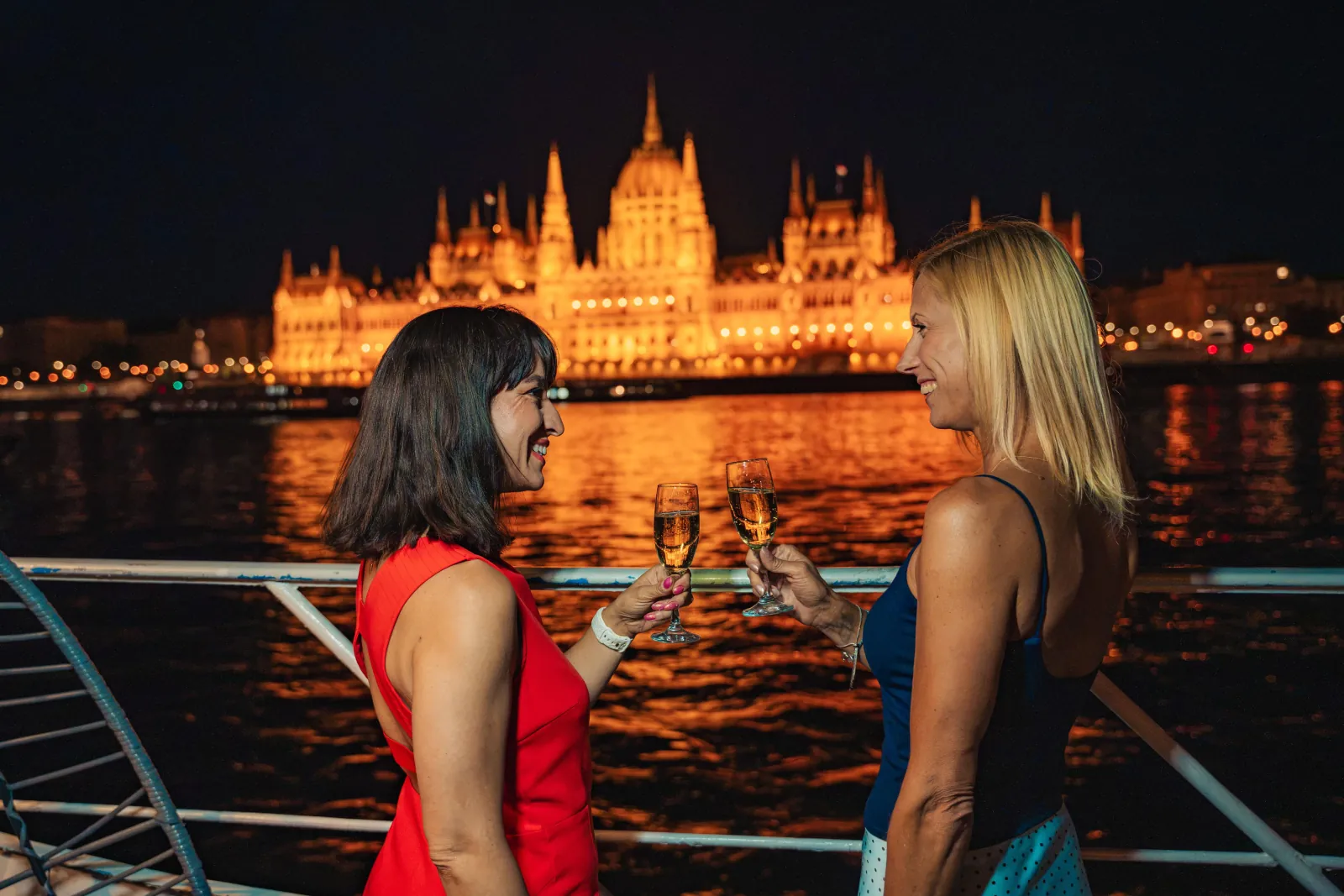 Two friends with drinks on deck, the Parliament lit behind